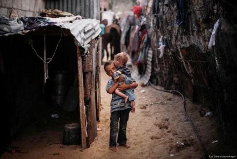 طفل يحمل شقيقه الصغير في أحد مخيمات قطاع غزة-تصوير APA البنك الدولي: انهيار وشيك في غزة