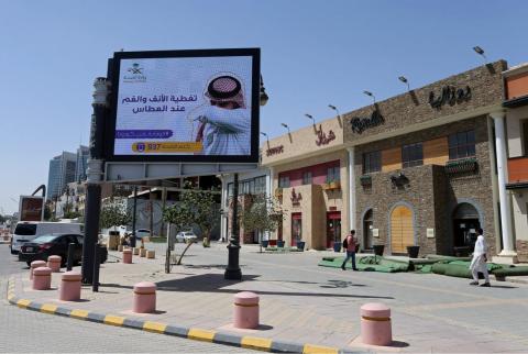 مشاة بالقرب من لافتة تحمل تعليمات للوقاية من فيروس كورونا في أحد شوارع العاصمة الرياض-تصوير رويترز السعودية ترفع ضريبة القيمة المضافة لثلاثة أمثالها ضمن إجراءات تقشف