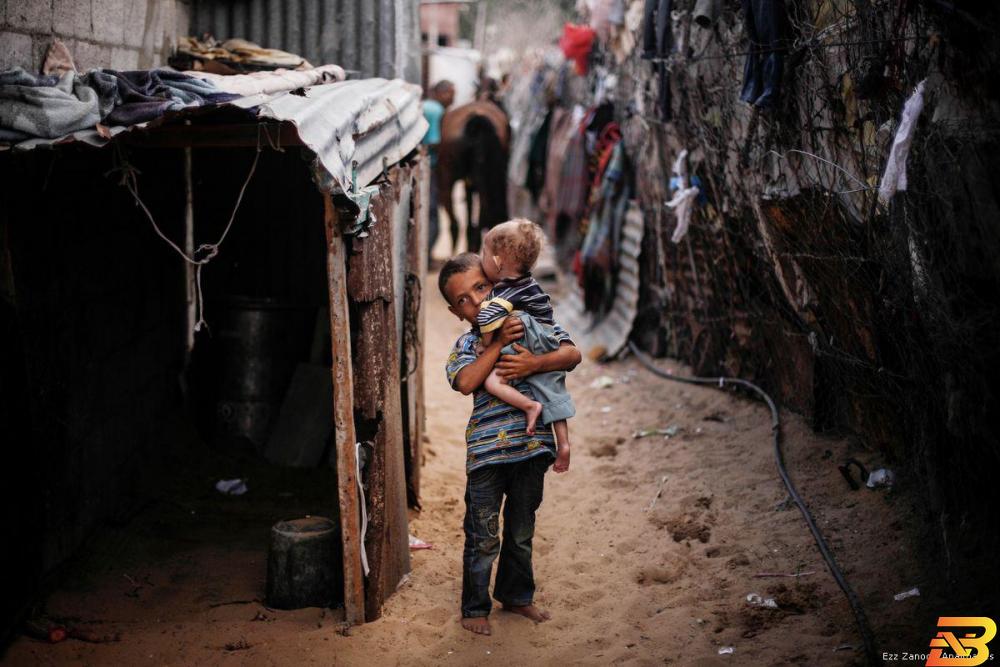 طفل يحمل شقيقه الصغير في أحد مخيمات قطاع غزة-تصوير APA البنك الدولي: انهيار وشيك في غزة