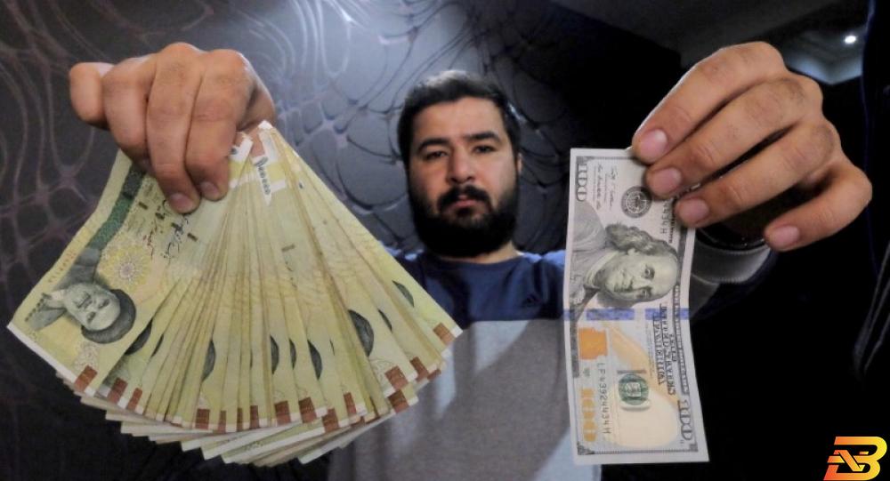 عامل بشركة صرافة يعرض ورقة نقدية فئة مئة دولار وما يعادلها بالريال الايراني في طهران-أرشيف رويترز. إيران تخفف قواعد الصرف الأجنبي أملا في دعم عملتها قبل العقوبات