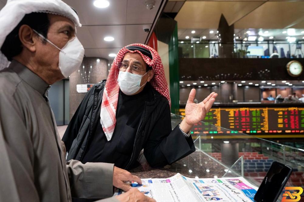 رجلان يضعان كمامات في بورصة الكويت-تصوير رويترز الكويت تستورد ملايين الكمامات الطبية لتوزيعها على المواطنين