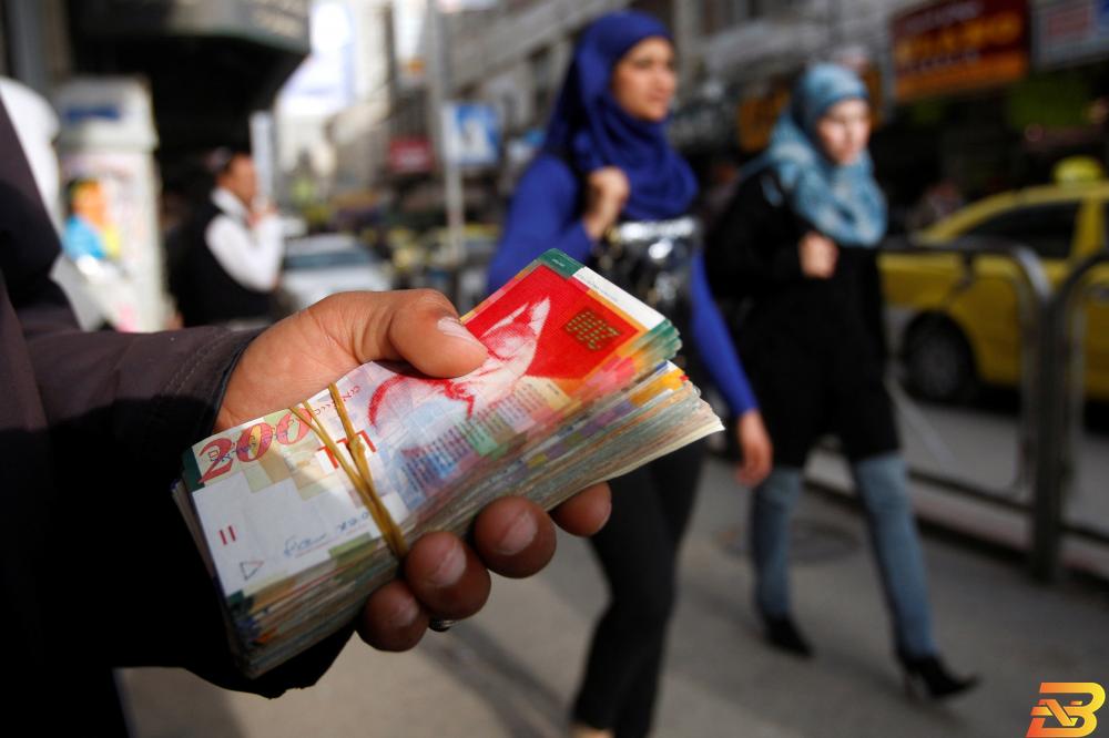 رجل يعمل في مجال الصرافة يحمل رزمة من الأوراق النقدية في رام الله-أرشيف وكالات ترحيب بتأجيل أقساط القروض وتحفظ على تعليق تصنيف الشيكات