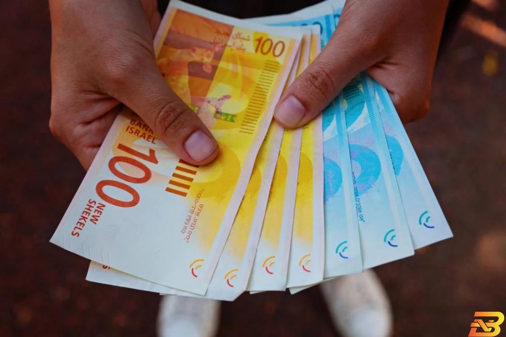 صورة توضيحية-رجل يحمل أوراق نقدية من فئتي 100و 200 شيكل-تصوير وكالات الناطق باسم الحكومة يتحدث عن موعد صرف الرواتب