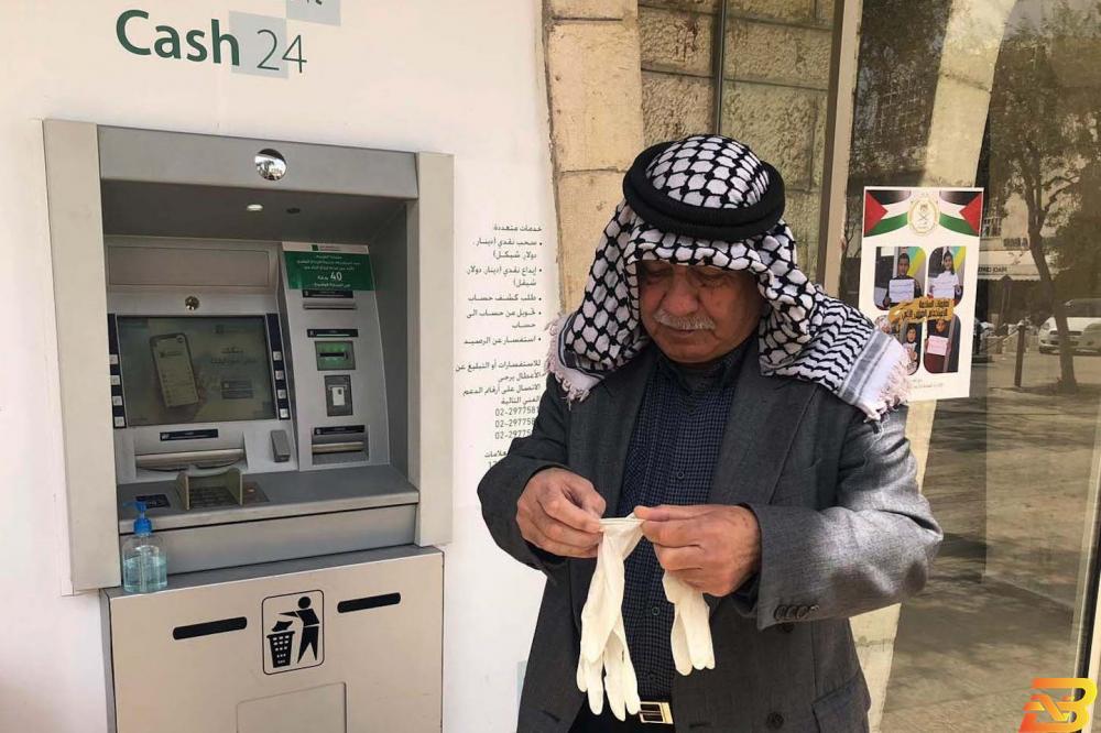 مواطن في بيت لحم يقوم بإرتداء كفوف طبية قبل استخدام الصراف الآلي التابع لأحد البنوك في ظل جائحة كورونا-تصوير أحمد مزهر تقديرات: تراجع النمو الاقتصادي 6% إذا استمرت أزمة كورونا 6 أشهر