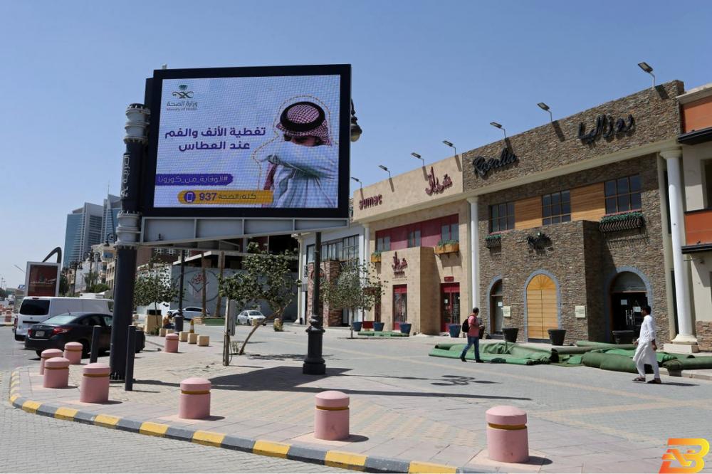 مشاة بالقرب من لافتة تحمل تعليمات للوقاية من فيروس كورونا في أحد شوارع العاصمة الرياض-تصوير رويترز السعودية ترفع ضريبة القيمة المضافة لثلاثة أمثالها ضمن إجراءات تقشف