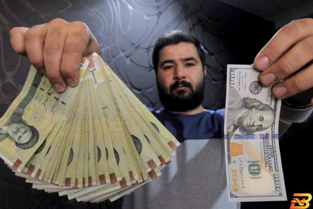 صورة من أرشيف رويترز لرجل يعمل في الصرافة يعرض عملة ورقية من الدولار الأمريكي (إلى اليمين) وبعض الأوراق المالية من الريال الإيراني (إلى اليسار) في طهران. الريال الإيراني يهبط لأدنى مستوى على الإطلاق أمام الدولار