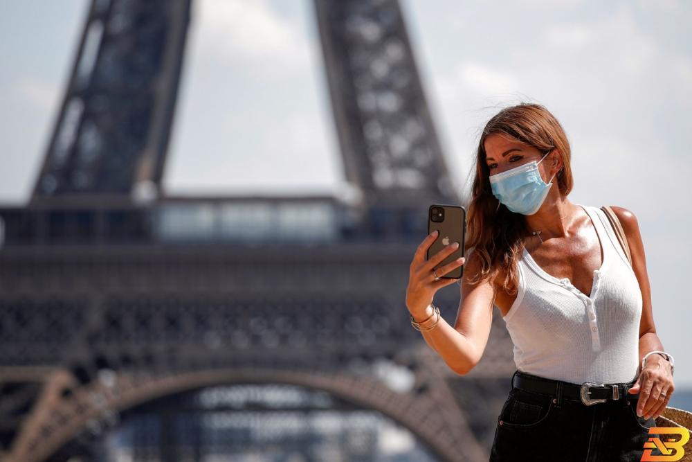 سيدة ترتدي كمامة تلتقط صورة أمام برج إيفيل في باريس-تصوير وكالات انهيار السياحة العالمية .. 730 مليار دولار الخسائر في 8 أشهر