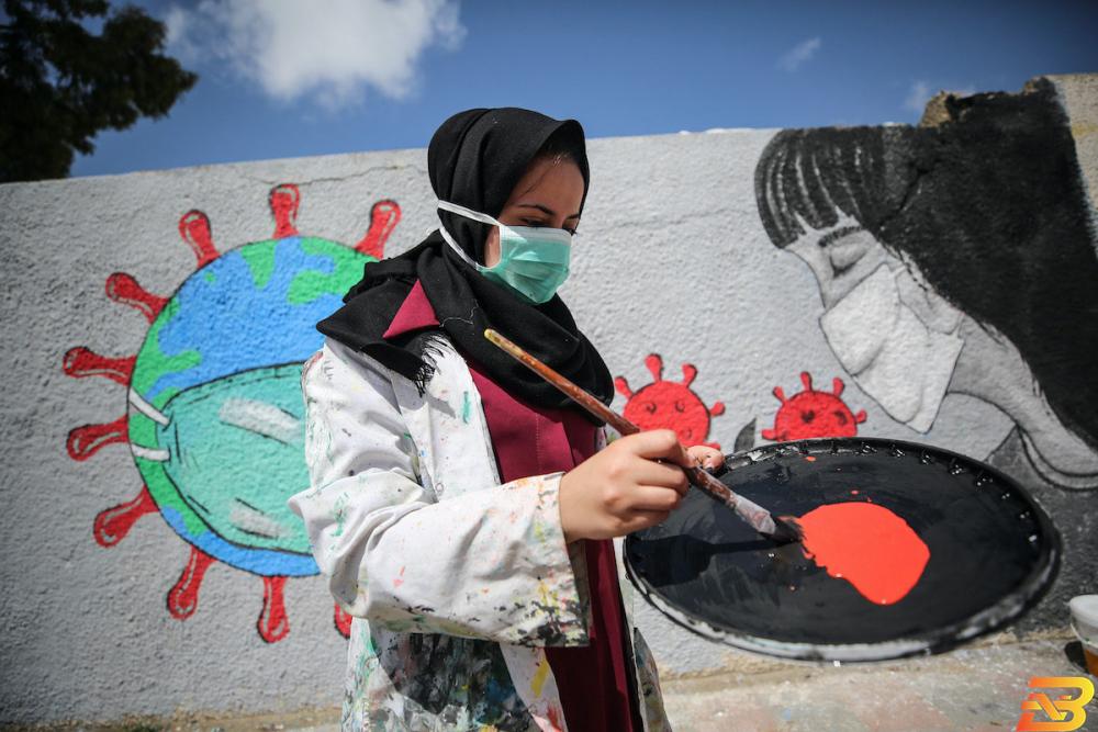 فنانة فلسطينية ترسم جدارية في غزة للتوعية بإجراءات الوقاية من فيروس كورونا-تصوير الأناضول 19 وفاة و1595 إصابة جديدة بفيروس كورونا